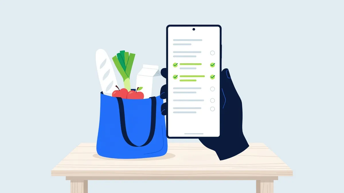 A hand holds an Android phone with a shopping list above a full shopping bag on a kitchen table.